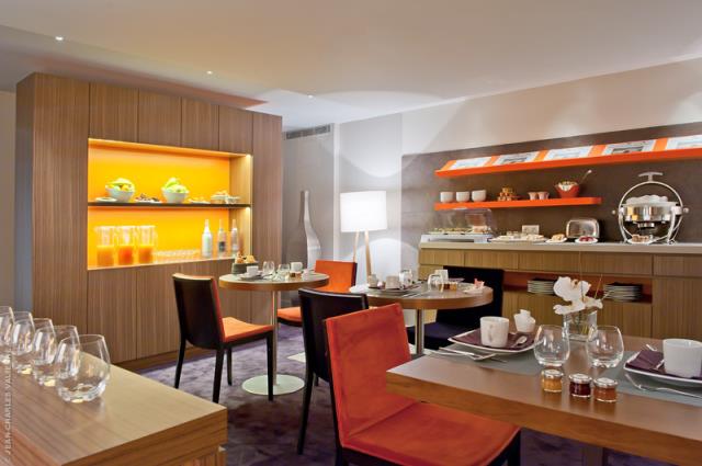 La salle de petit déjeuner, en sous-sol, est un lieu chaleureux et intime, avec des chaises dont les assises sont orange et prune.