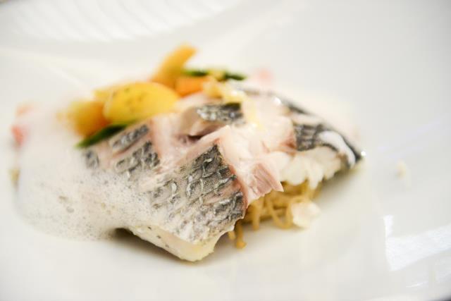 Filet de bar cuit doucement et servi sur un bouillon épicé au lait de coco et combava, Tomate confite et poêlée de légumes nouveaux.