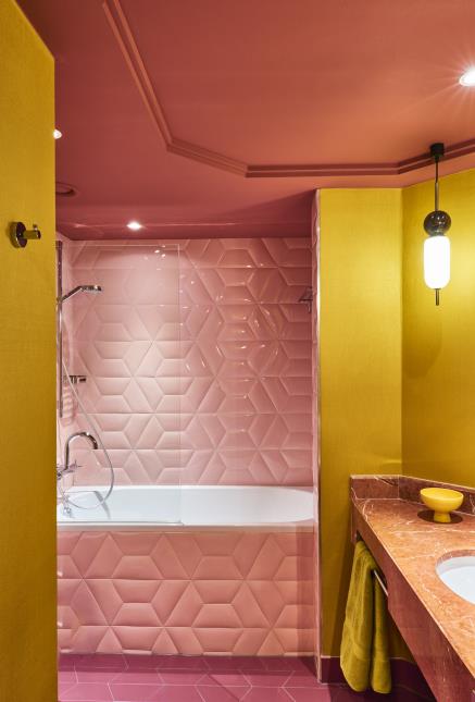 Salle de bains parée de céramique graphique rose asymétrique, en accord avec les vasques en marbre d'origine, qui ont été conservées.