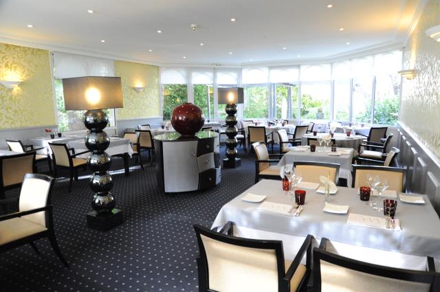 La salle du restaurant avec de larges baies vitrées qui donnent sur le jardin et les terrasses