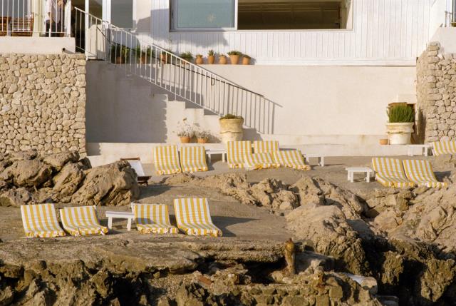 Posé sur un rocher, Tuba, réserve quelques transats à la clientèle de l'hôtel. Leurs rayures jaunes et blanches contrastent volontairement avec le bleu très présent du ciel et de la mer.