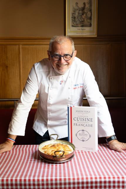 Joseph Viola devant son gratin de macaronis et son livre de recettes des plats traditionnels français.