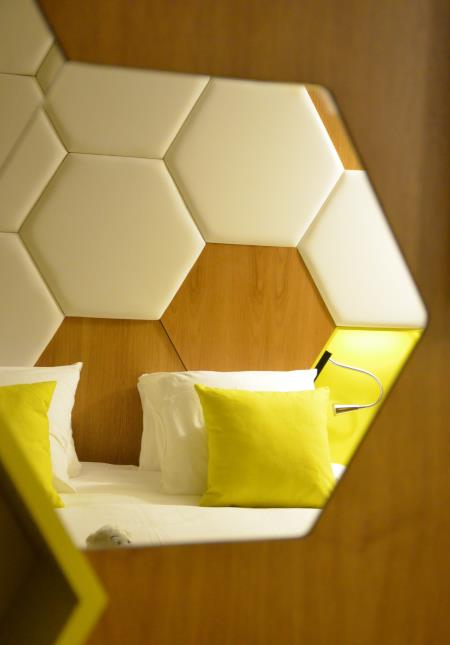 L'alvéole est partout. Ici, reflet de la tête de lit dans le miroir hexagonale du bureau d'une chambre couleur jaune