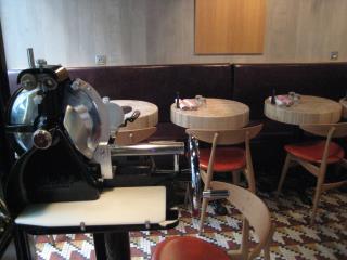 Trancheuse à l'entrée, tables en bois rappelant un billot de boucher, couteaux plantés dans une...