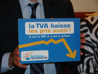 Hervé Novelli présentant la vitrophanie que les restaurateurs répercutant la baisse de TVA selon les modalités du contrat d'Avenir pourront apposer sur la vitrine de leur restaurant afin d'informer leur clientèle