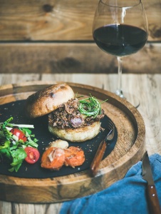 Un hamburger à l'effilochée de porc et à la salade de chou, avec un verre de vin rouge.