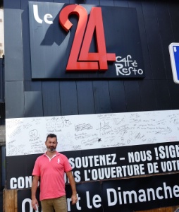 Jérôme Delpeuch pose devant Le 24 Resto et une affiche incitant à signer la pétition de défense du restaurant.
